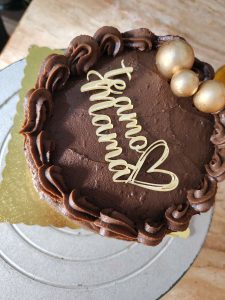 Chocolate cake with “I love you mom” written in icing and decorated with flowers and golden details.