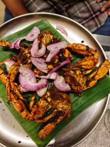 
A silver plate features a serving of crab seasoned with spices, topped with sliced red onions.
