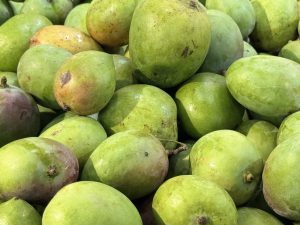 A pile of fresh green mangoes with orange-red hues.