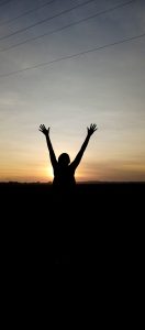 a person with lifted arms in the sunset. 
