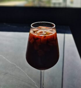 A glass of dark fruit mocktail filled with diced fruits, resting on a sleek surface.