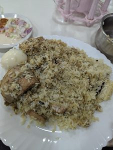 A white plate of aromatic biriyani with meat pieces and a boiled egg.