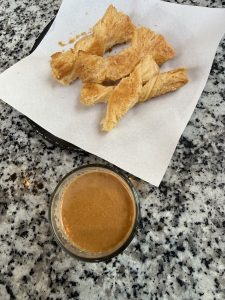Chiya and khari, flaky golden-brown pastries, are served on parchment paper with a small glass of creamy light brown tea.