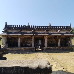 Ancient stone temple with weathered pillars and intricate roof carvings under a clear blue sky, conveying a sense of historical grandeur.