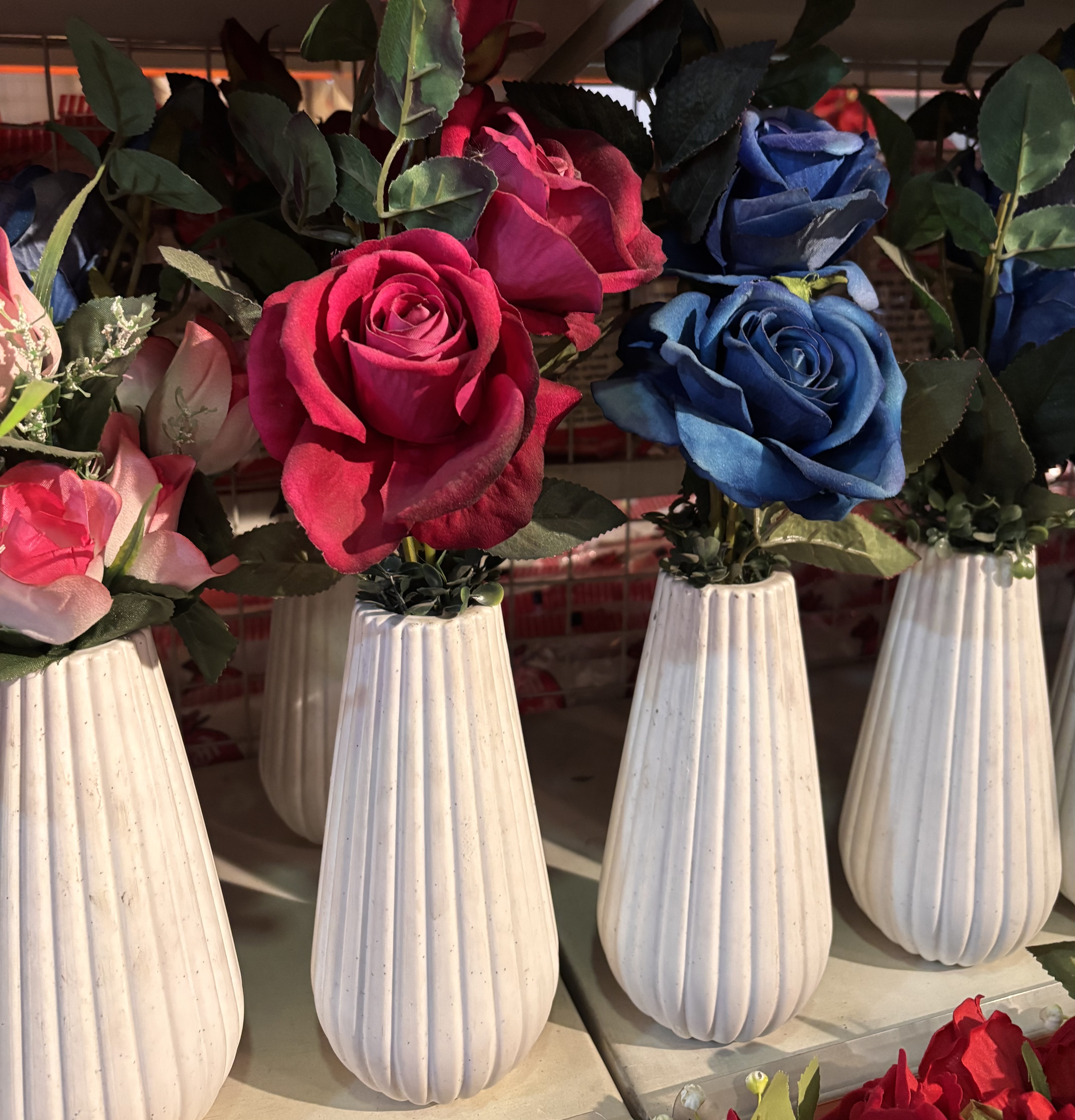 White ceramic vases with vibrant artificial roses in pink, red, and blue under warm lighting.