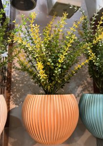 Vibrant yellow and green artificial plant in a textured orange vase, placed on a display shelf. 