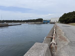 A calm waterfront with a concrete path and rusty railing along the water at Inage Seaside Park.