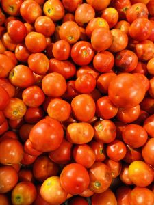 A vibrant pile of ripe red tomatoes fills the frame, showcasing a glossy texture and rich color.
