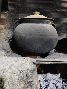 A traditional pot over a wood-fired stove conveys the warmth and essence of homemade cooking, surrounded by ashes and rustic textures that evoke tradition and flavor.