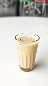 A glass of frothy light brown milk tea on a white surface.