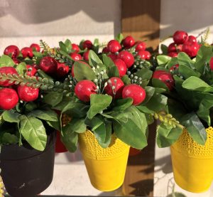 Vibrant artificial plants with red berries and green leaves in yellow and black pots on a shelf. 