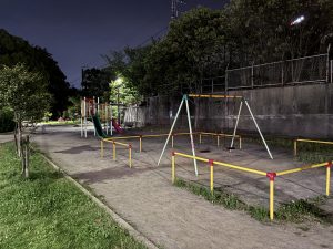 A quiet playground at night with colorful slides, swings, gravel paths, and trees creates a peaceful atmosphere at Shin-Chiba Park.
