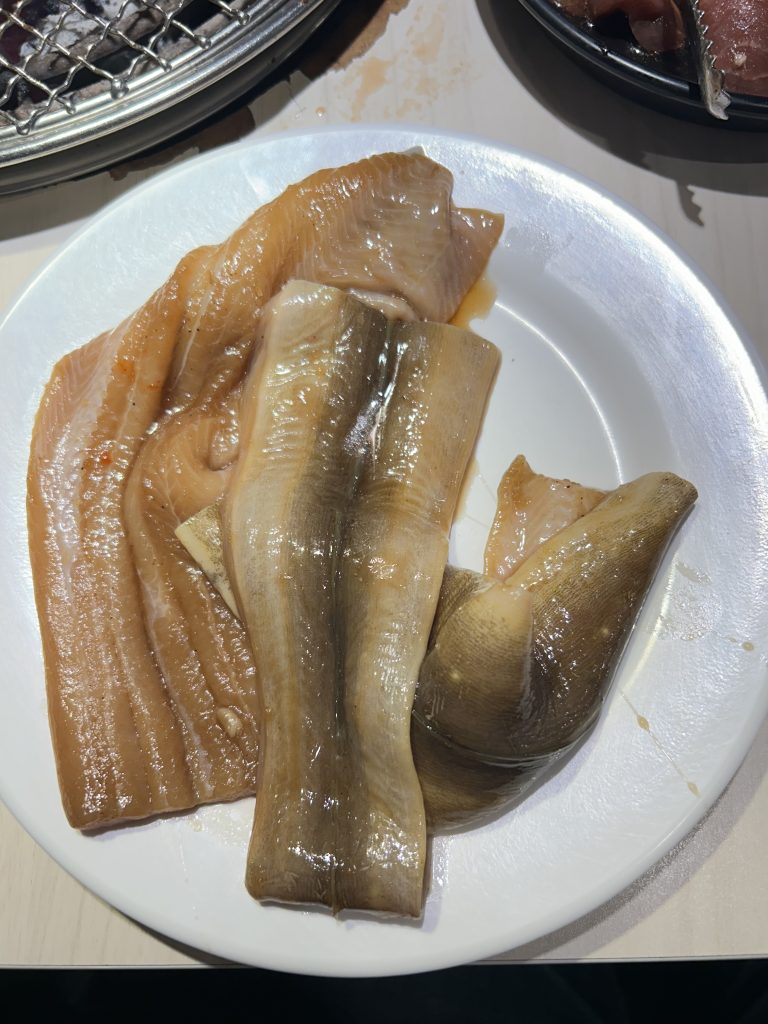 A white plate holds several pieces of fish fillets. The fillets are a mixture of colors, including light orange, light brown, and darker tan shades. The textures appear smooth and slightly glossy, indicating they might be marinated or seasoned.