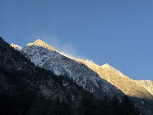 Snow-covered mountain peaks under a clear blue sky, with the sun casting a warm glow on the slopes.