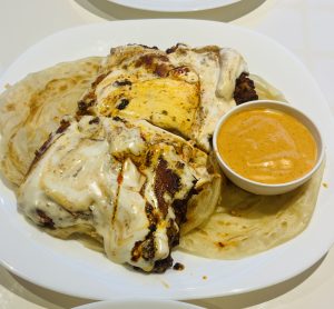 Creamy, spicy chicken on a flaky paratha is topped with melted cheese and drizzled with sauce