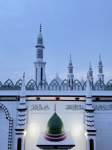 Mosque from top height view having green dome lookalike in front and Quran Verses written on the wall.