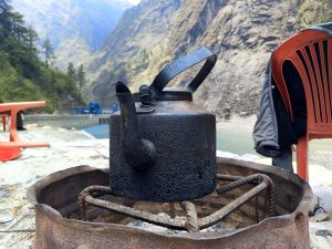 A worn black kettle sits on a metal stand outdoors beside a red plastic chair.