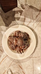 A white plate holds a serving of round, chocolate-covered desserts drizzled with white and dark chocolate stripes