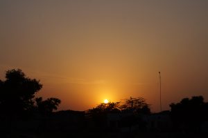 A serene sunset is captured, with the sun partially visible just above the horizon, casting a warm orange glow across the sky.