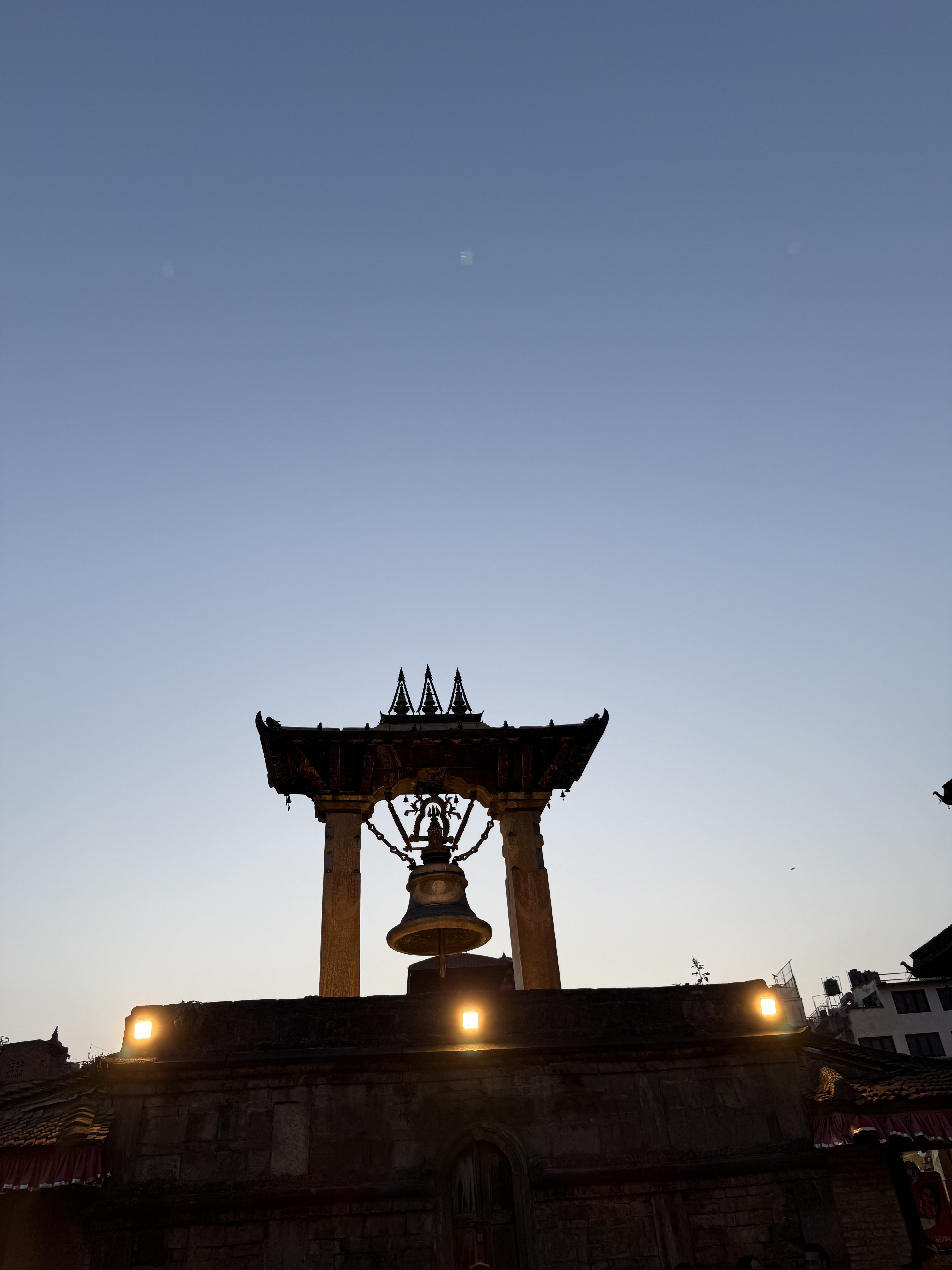 Historic bell tower silhouetted against a dimming sky at dusk, with warm lights illuminating the structure, creating a serene atmosphere.