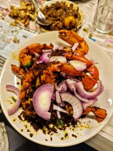 

A plate of spicy grilled Crab is topped with slices of red onion and garnished with green leaves.