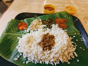 A banana leaf serves as a plate, showcasing a meal that includes a mound of white rice, accompanied by various sides