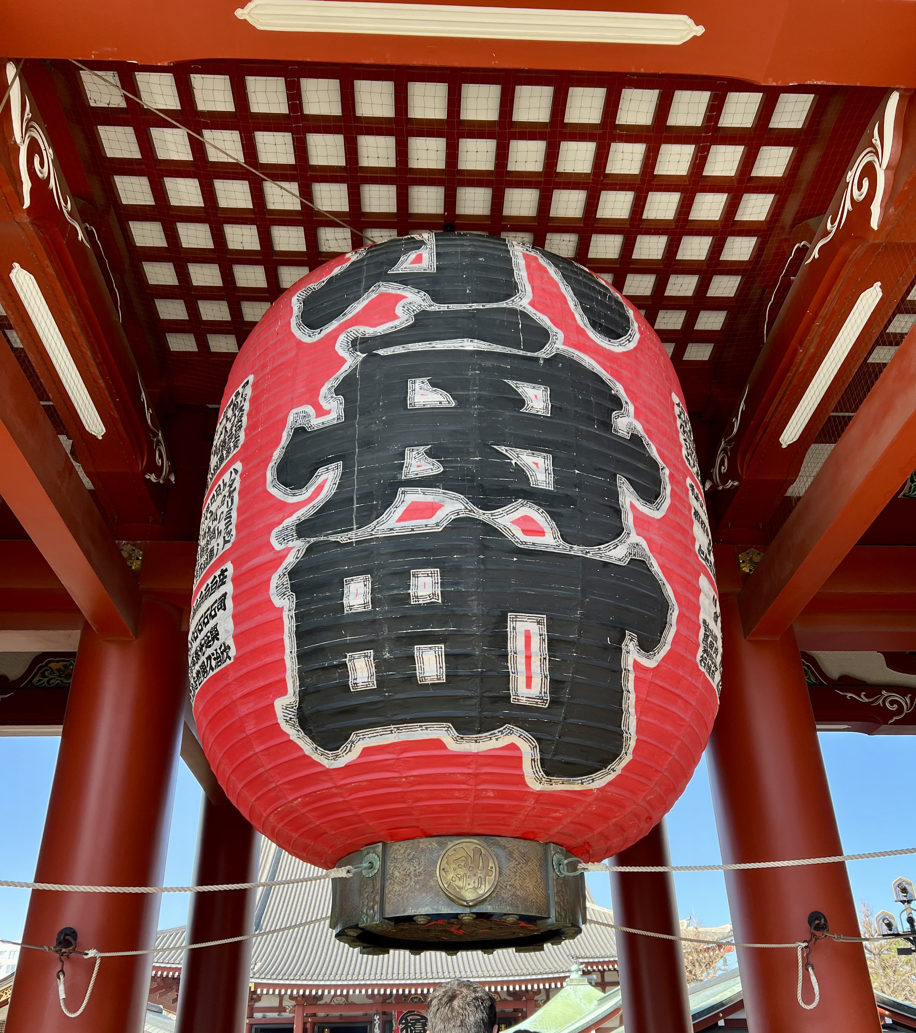 A large red paper lantern with black Japanese characters hanging under a temple gate.