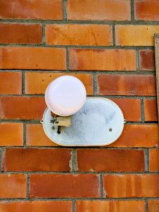 A white light fixture with a round bulb is mounted on a red brick wall. 