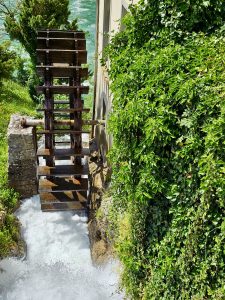 An old wooden water wheel turns beside fast-flowing water and green ivy-covered walls. This charming scene reflects the historic beauty near Rhine Falls, Switzerland.