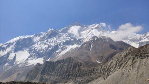 Snow-capped mountain under a clear blue sky with rugged slopes and scattered clouds, conveying a sense of majesty.