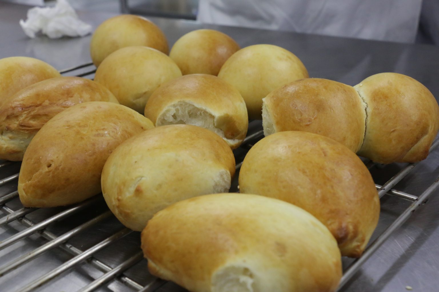 Plain golden-brown bread buns cooling on a metal rack in a kitchen.