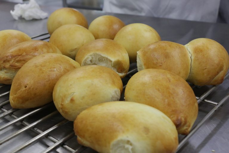 Plain golden-brown bread buns cooling on a metal rack in a kitchen.