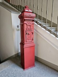 A beautifully preserved vintage red post box stands beside a staircase, showing classic old-world design and charm indoors in Turin (Torino), Italy.