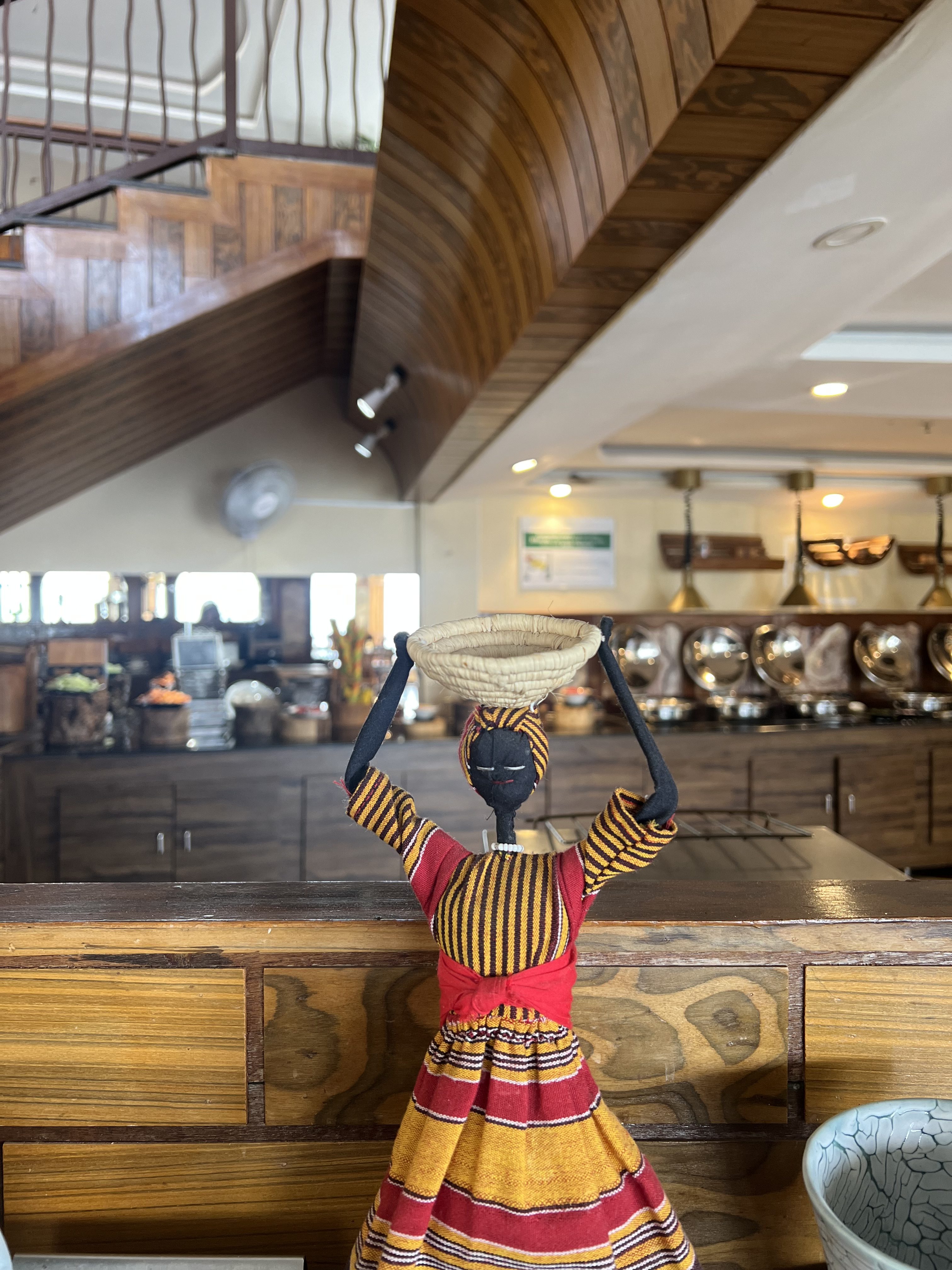 A colorful, handmade cloth doll wearing a striped dress and balancing a woven basket on her head.