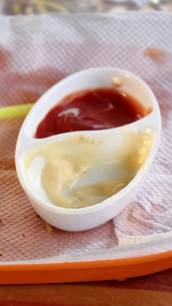 A white dipping dish with ketchup and mayonnaise sits on a napkin, with a single french fry on the side.