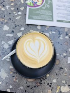 A cup of Latte coffee in a black cup placed on the table. There's a heart formed in the foam.