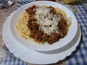Spaghetti with ground beef and cheese on top in a white bowl.