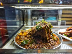 A close-up of beef ribs in a metal plate, topped with green curry leaves.