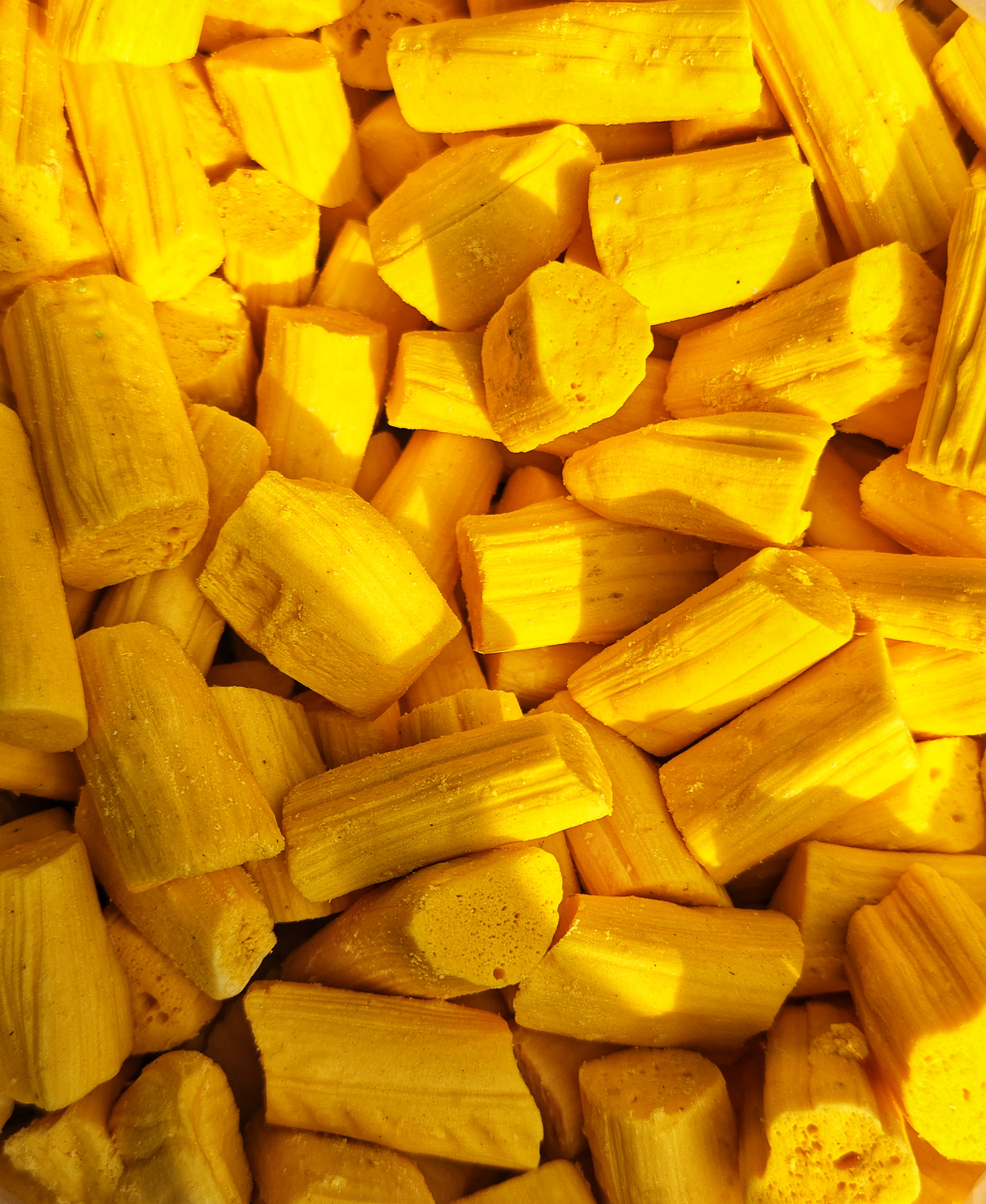 A close-up of a pile of bright yellow cylindrical candy pieces of varying shapes and sizes.