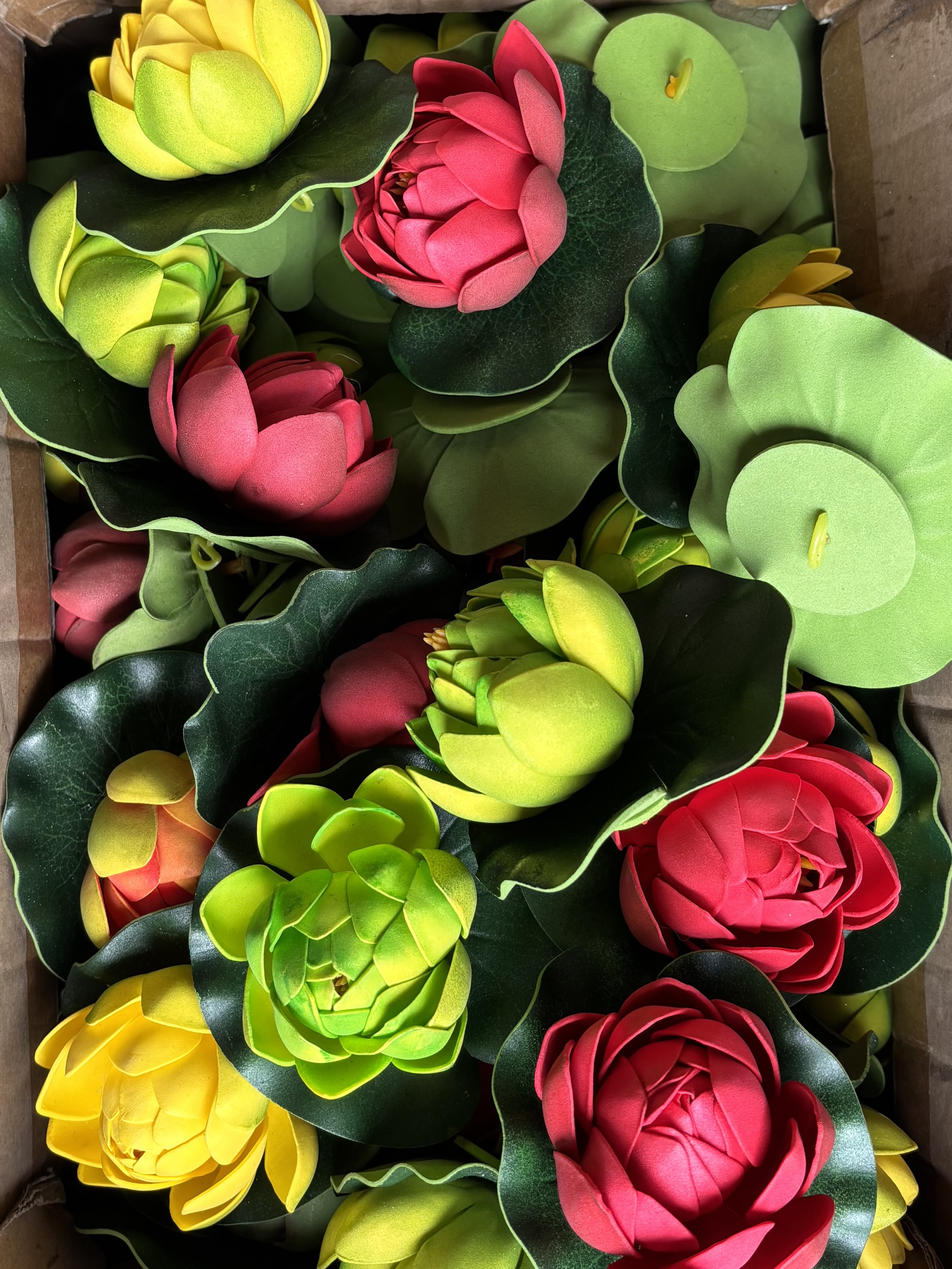 Colorful artificial lotus flowers in yellow, pink, and green with green leaves.