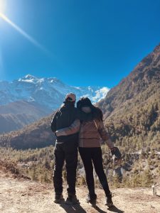 A couple stands arm in arm, gazing at snow-capped mountains under a clear blue sky.