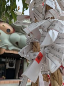 Traditional omikuji fortune papers tied to a sacred straw rope at Namba Yasaka Shrine in Osaka, Japan. The folded fortunes flutter beside the shrine’s iconic lion-head stage, symbolizing prayers, hopes, and the Shinto practice of leaving predictions behind to seek good fortune and spiritual guidance.