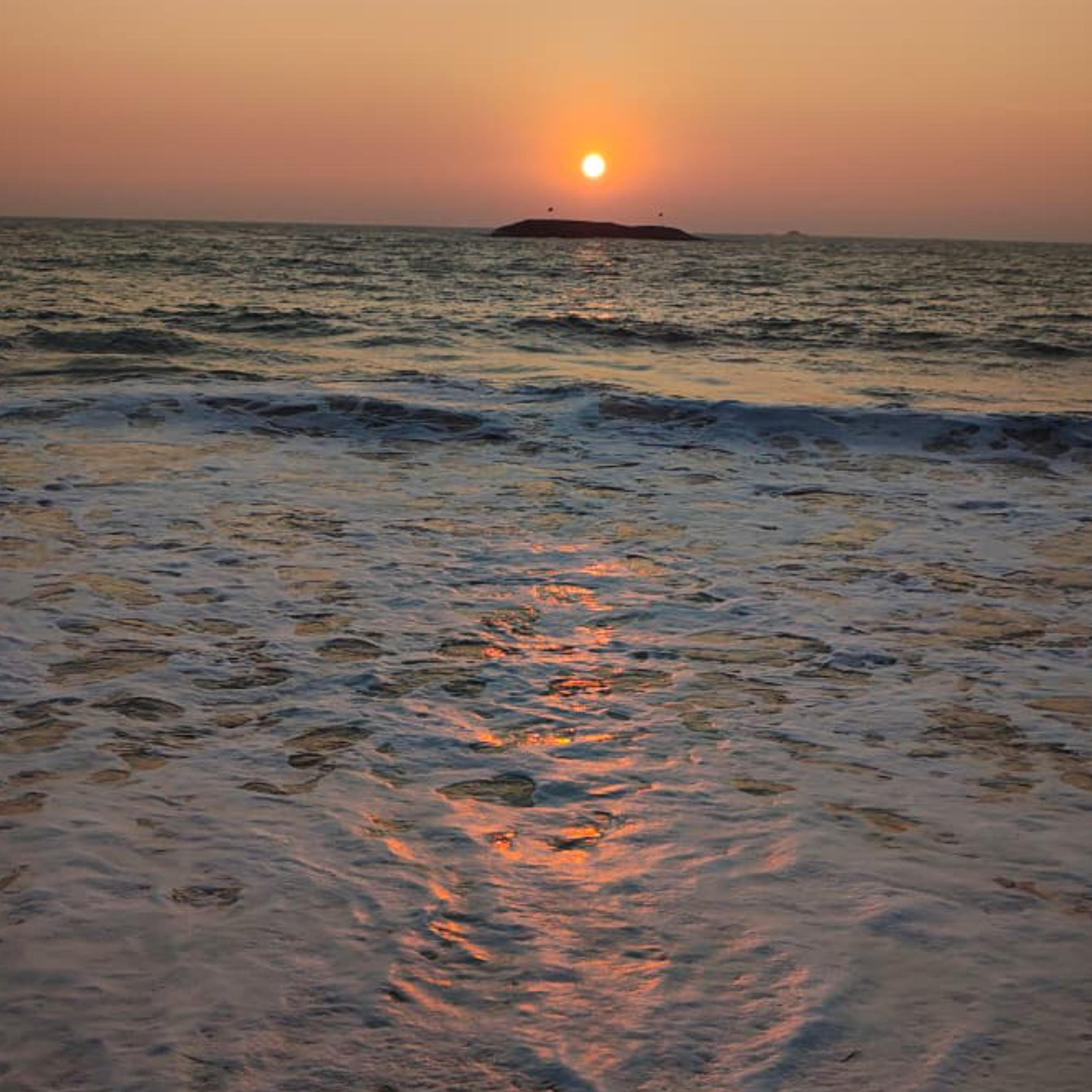 Sunset over the ocean with a vibrant orange sky.