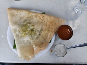 A traditional South Indian masala dosa served on a white plate with flavorful sambar and fresh coconut chutney. This crispy, golden rice and lentil crepe is filled with seasoned potato masala, offering a delicious combination of texture and authentic Indian flavors. A popular choice for breakfast, lunch, or dinner.
