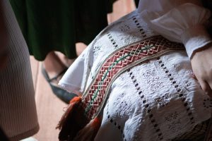 Close-up from above of traditional Lithuanian folk clothing with a white embroidered apron and a red-and-green woven sash.

