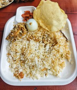 Generous plate of fragrant biryani rice topped with a boiled egg, crispy papadum and spicy pickle on the side 