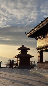 Ornate pagoda temples bathed in warm golden sunset light with dramatic clouds and misty mountain silhouettes stretching to the horizon 