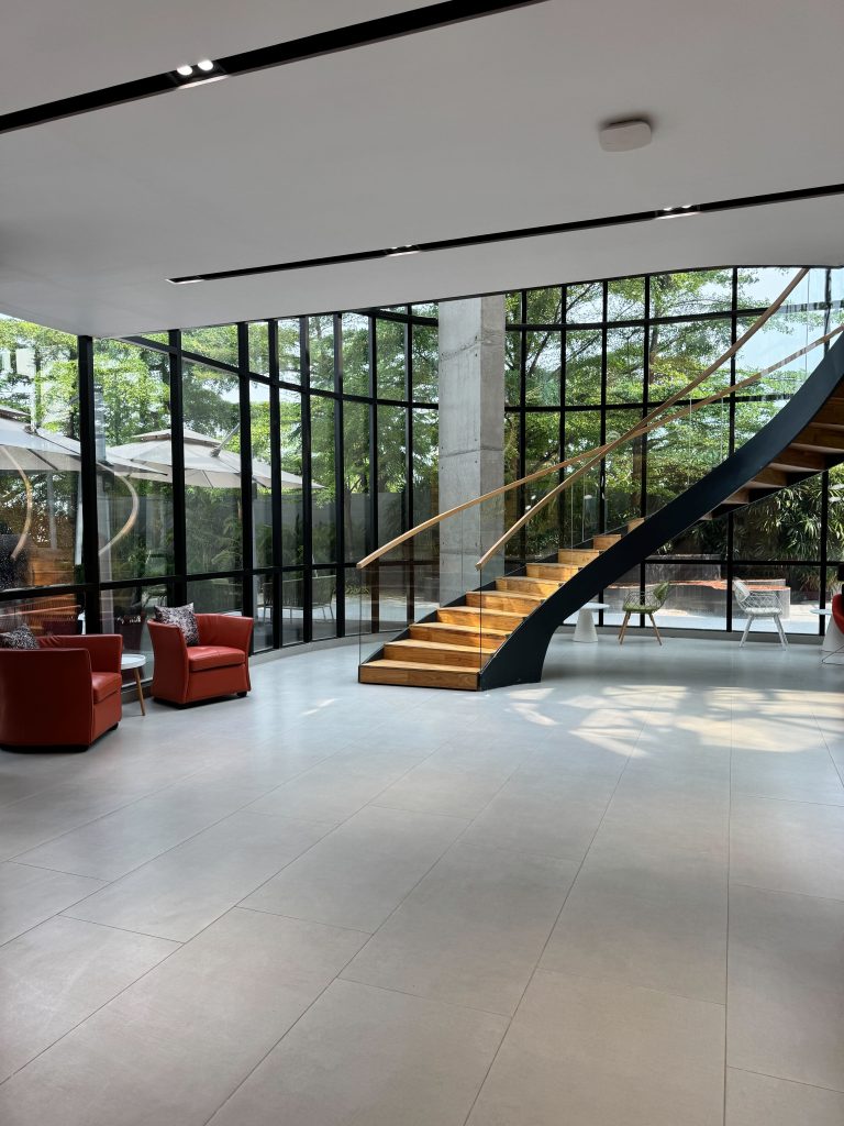 A modern lobby with a curved wooden staircase and floor-to-ceiling windows.