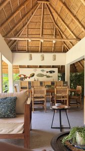 A spacious open-air dining area with a traditional thatched roof, wooden furniture, woven chairs, and tropical décor.