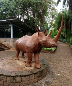 A large outdoor sculpture of a rhinoceros with an exceptionally long horn, meticulously constructed from welded panels of sheet metal. 